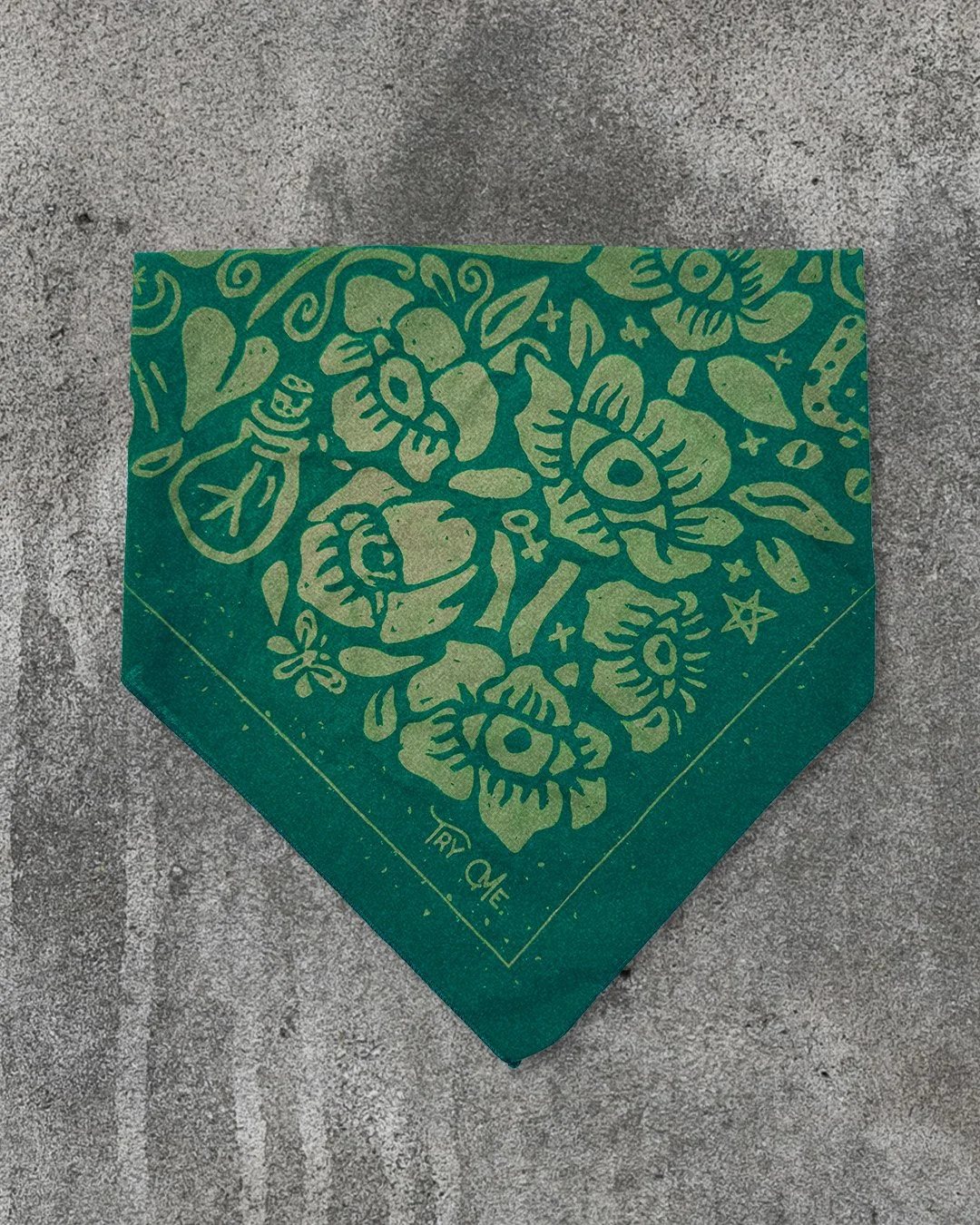 Alt text: Poisoner’s Garden bandana by Sugar Camp in moss green, folded into a triangle on concrete background.