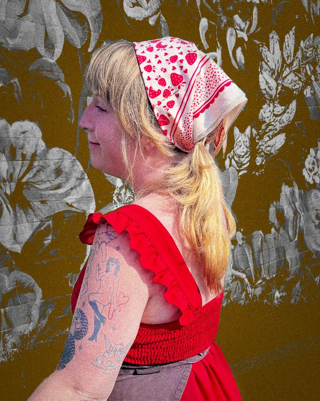 The side of a young woman in a frilly red dress wearing an Eat the Rich Sugar Camp cream bandana with strawberries on it. She is in front of a cat mural.