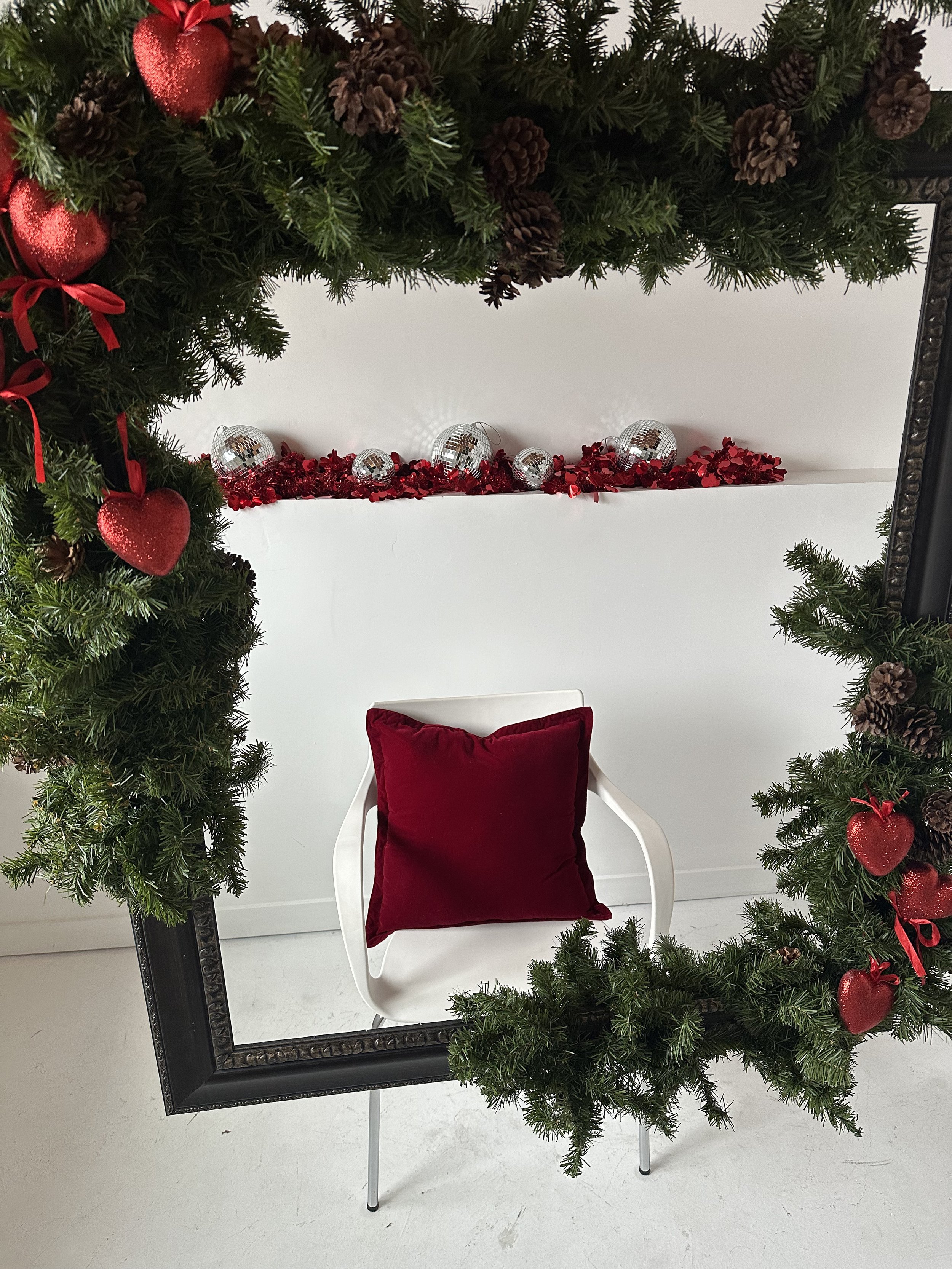 Valentine’s photoshoot set in Edmonton studio featuring a garland-wrapped hanging frame, red heart accents, and disco ball details for romantic, editorial portraits.