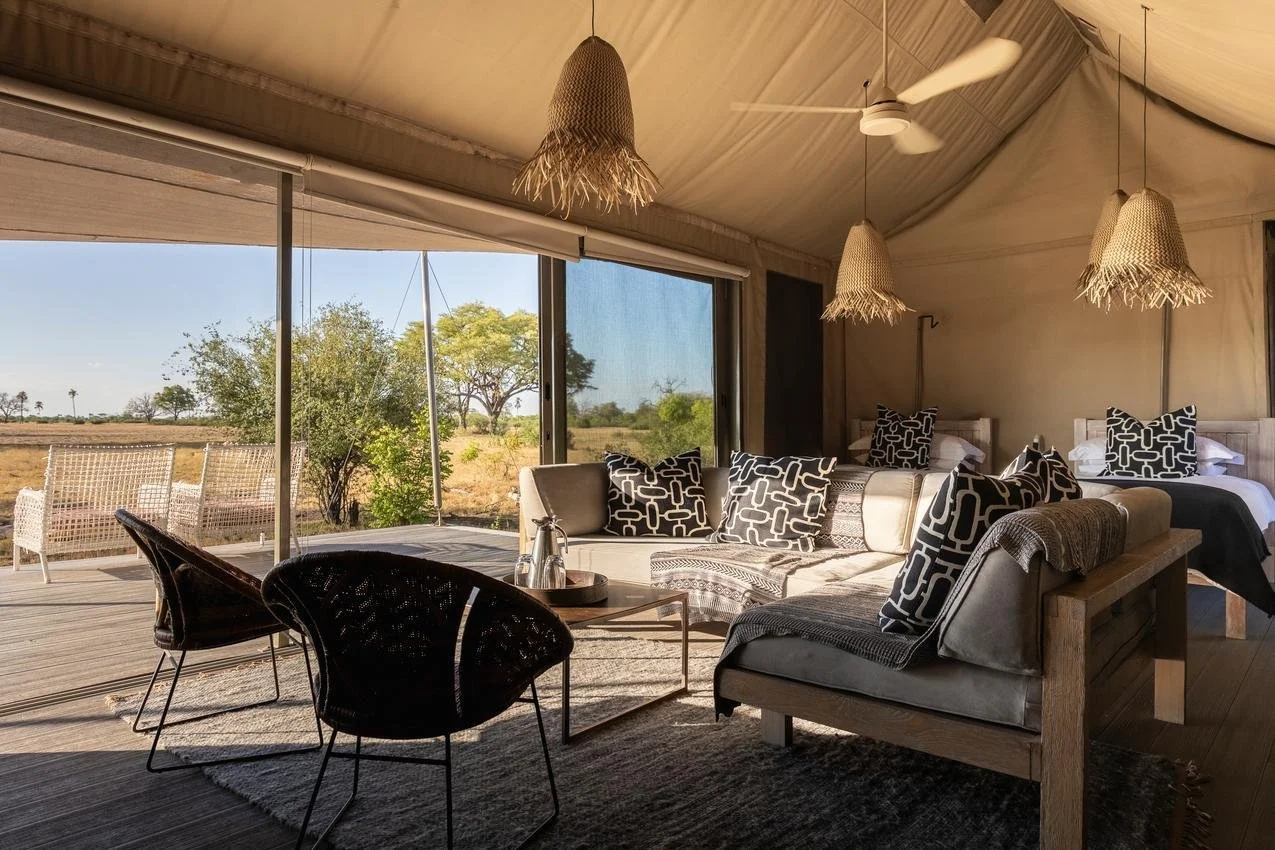 Interior view of a spacious tent with a seating area and a bedroom, overlooking an outdoor landscape with trees and open fields.