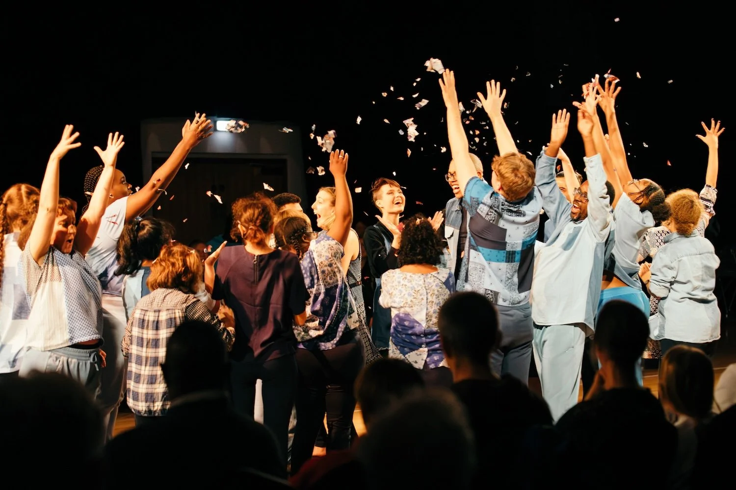 Group of people celebrating on stage with confetti and raised hands, smiling and enjoying a joyful event.