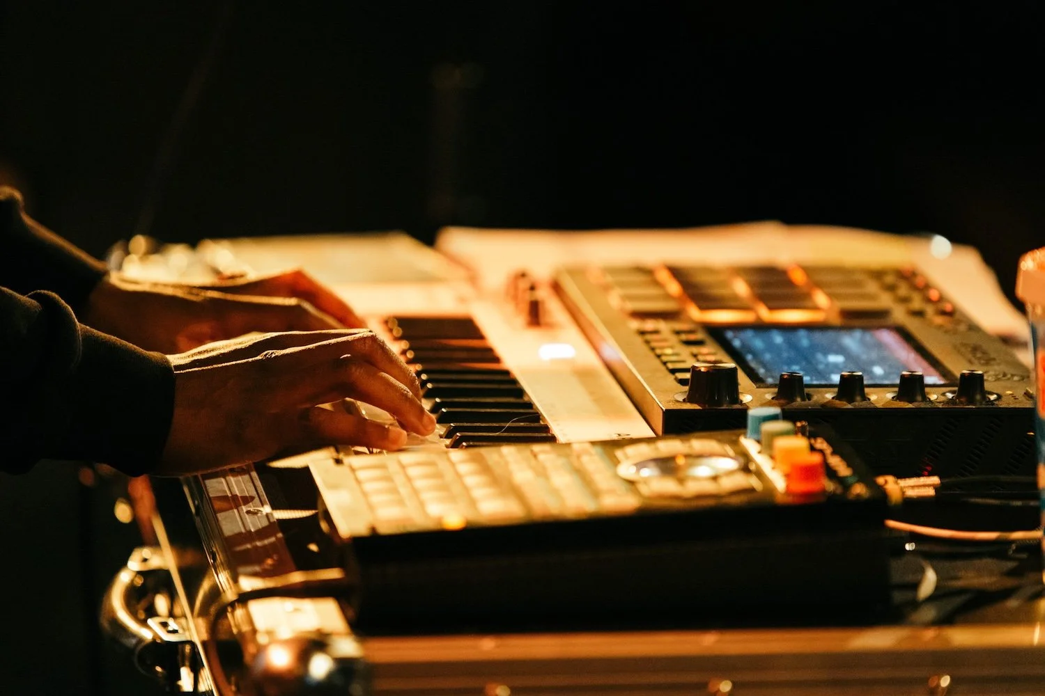 Hands operating a digital music controller or synthesizer in a dark setting.