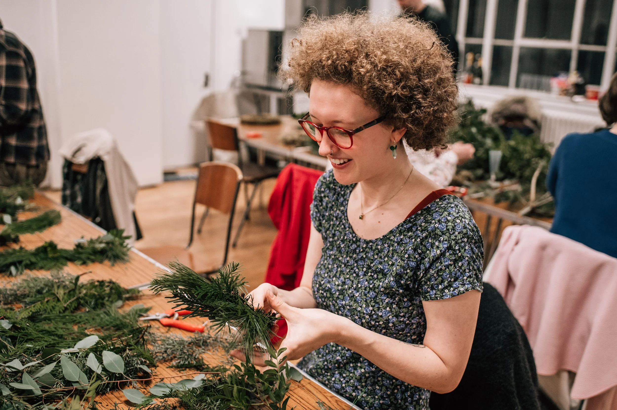 A woman wearing glasses is using foliage to make a wreath