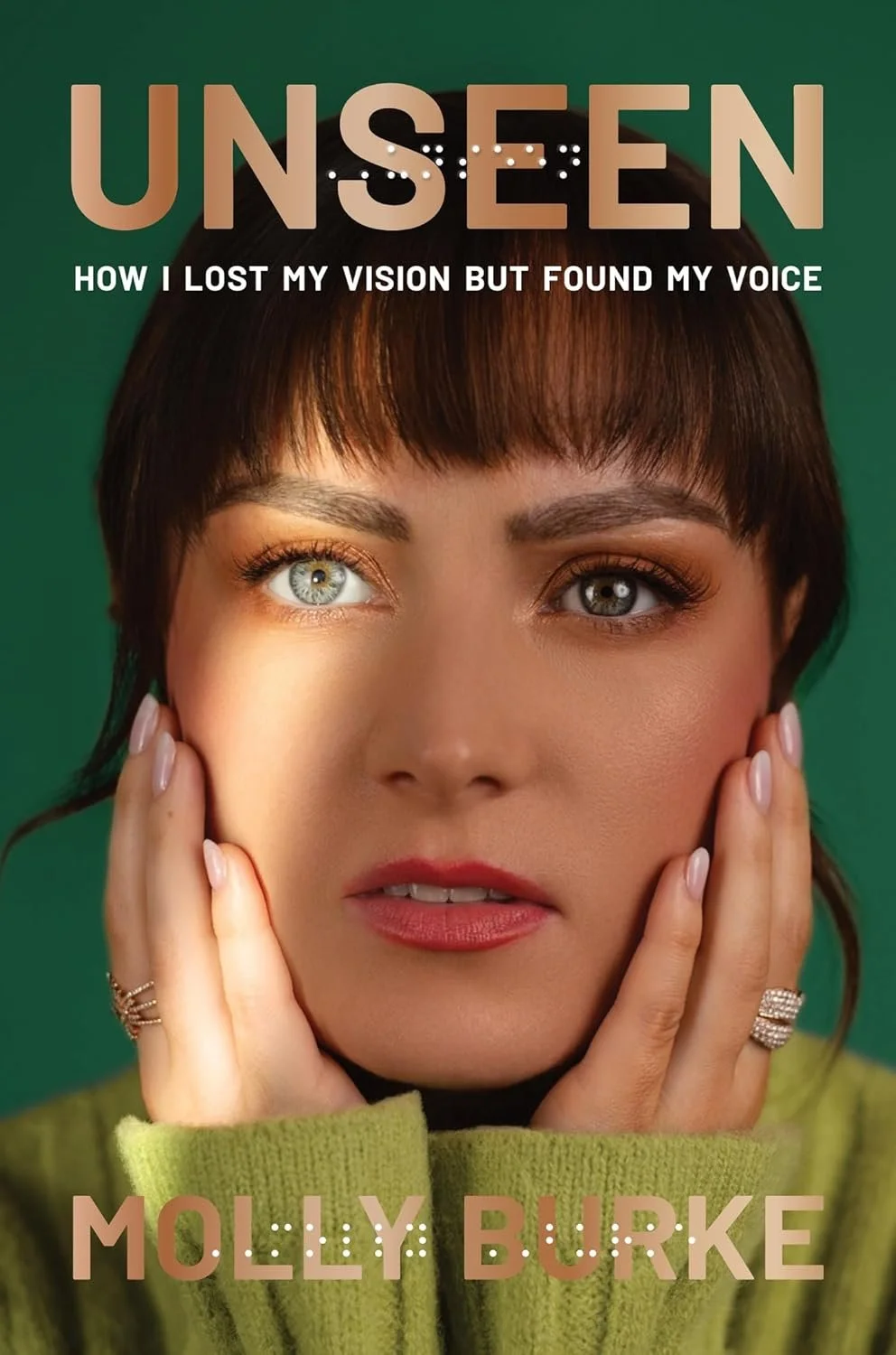 Molly's book cover for Unseen: How I Lost My Vision But Found My Voice. The cover has a green background with bold, golden text and a closeup portrait of Molly with her hands against her cheeks. A slash of light rakes across her right eye.