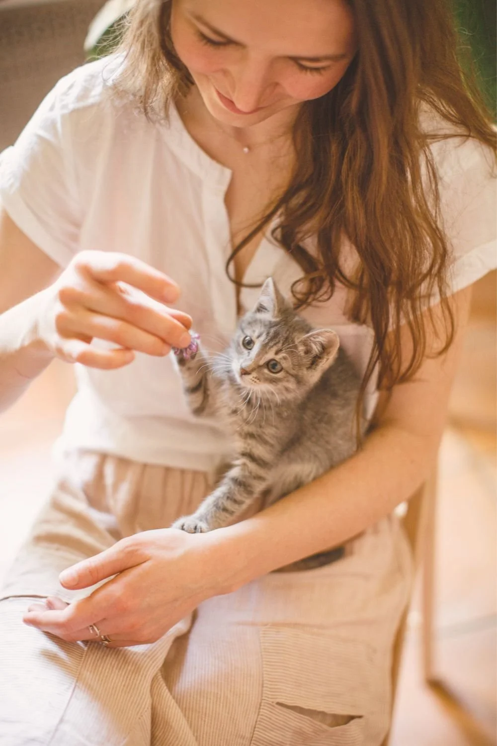 A woman is lovingly holding her little tabby kitten.