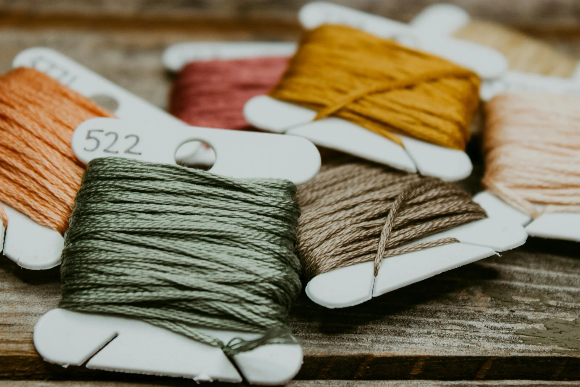 Various colored embroidery floss wound on white bobbins placed on a wooden surface.