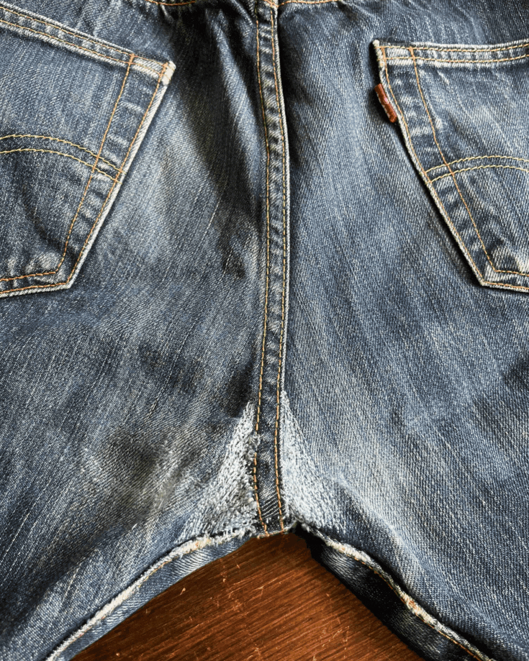 Close-up of the back of a pair of worn blue jeans showing pockets and faded areas.