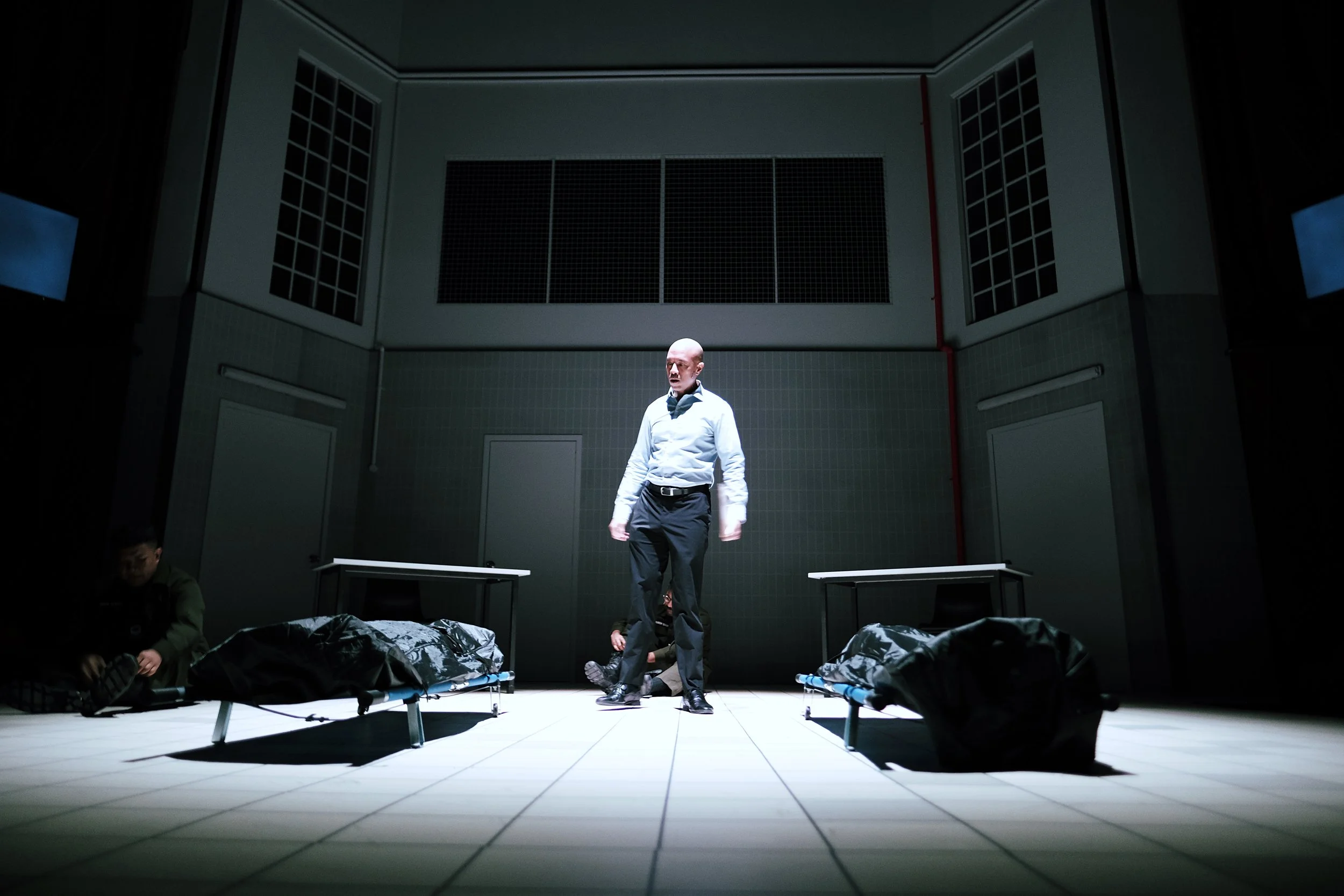 Still image from Scene 1 of Charged. LTC Victor de Souza is centrestage, looking at 2 bodybags containg the remains of 2 dead soldiers.