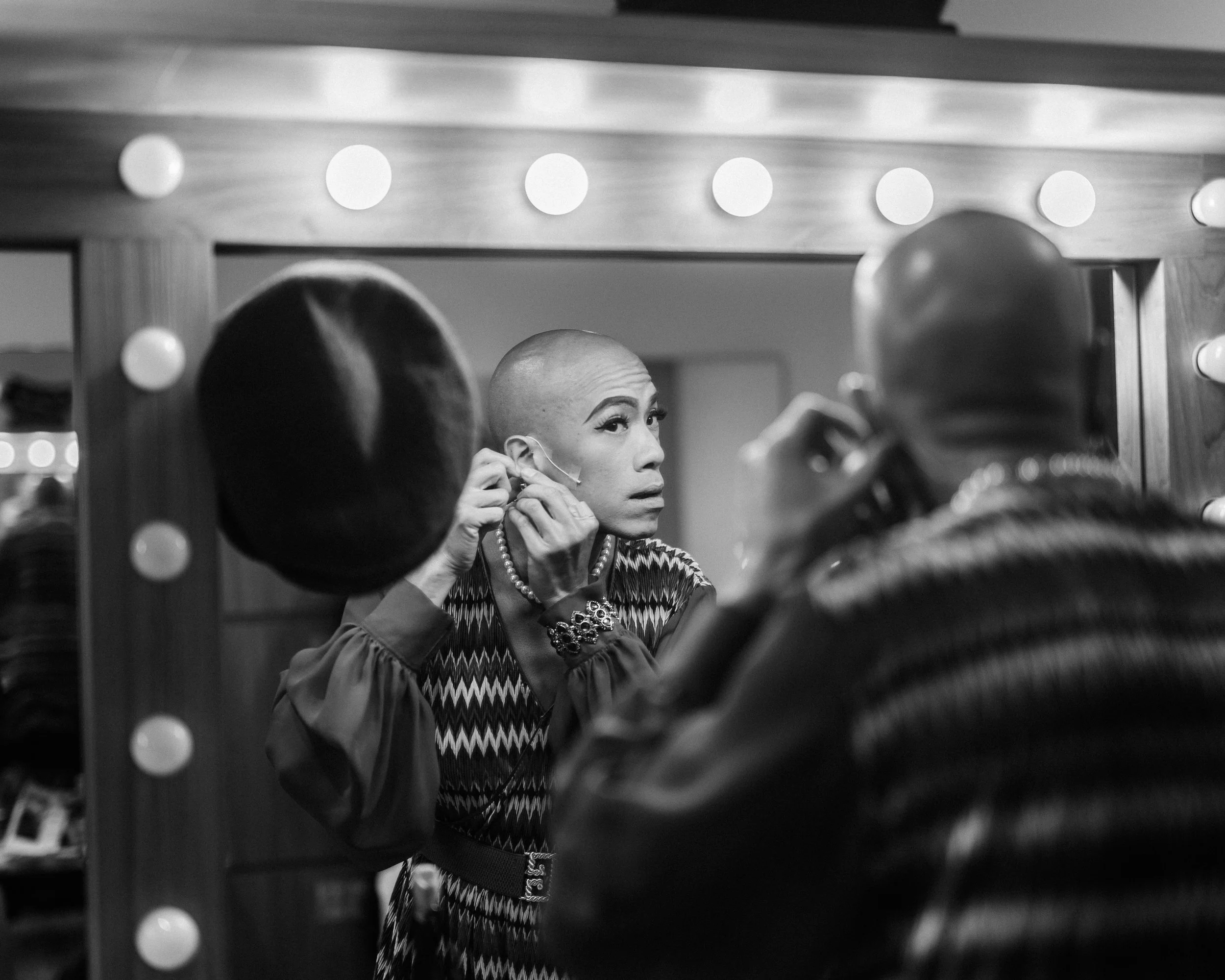 Brendon Fernandez in the dressing room, putting on an earing, preparing to play Bridget Tessensohn from scene 1975.