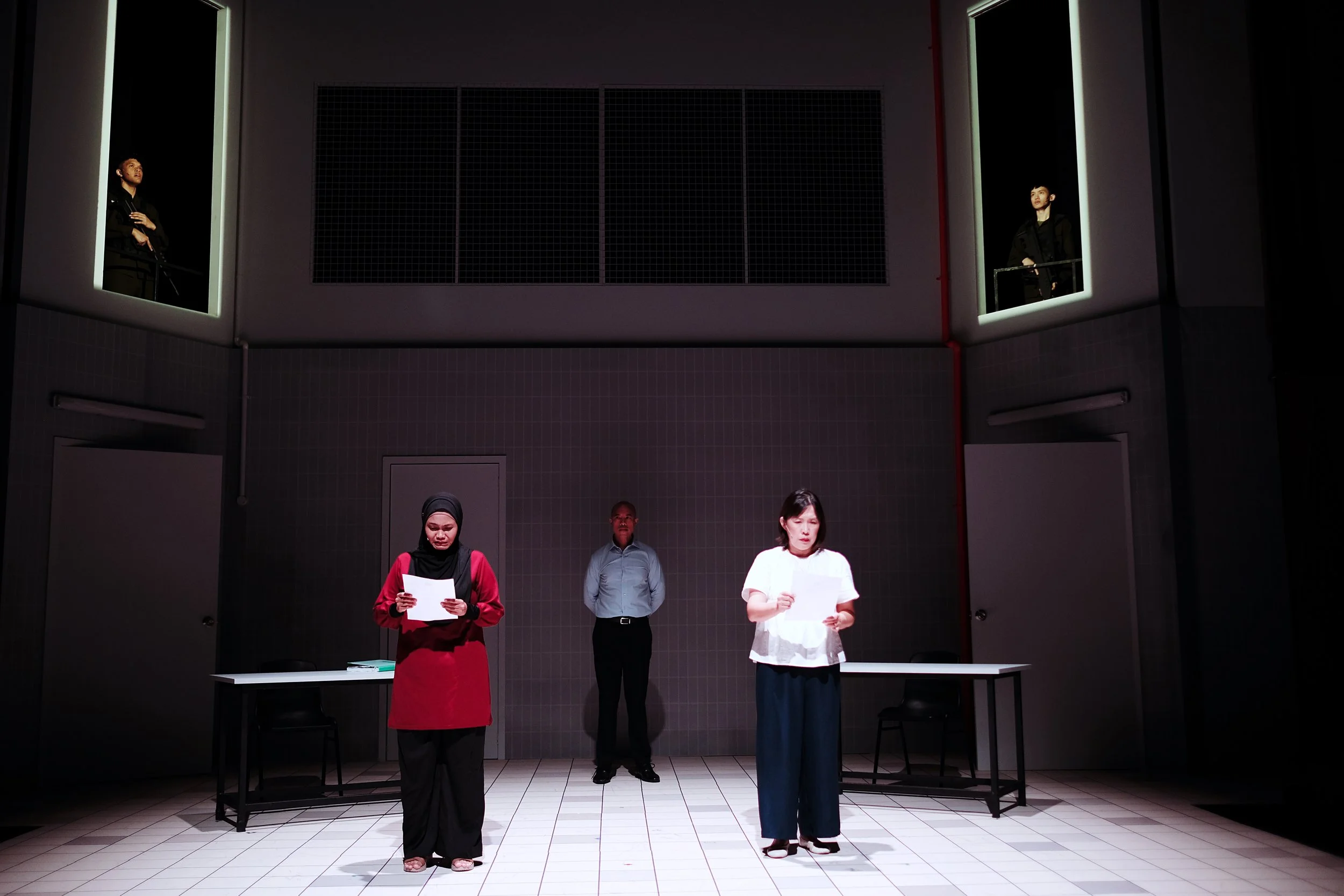 Production still from the final scene of Charged by Teater Ekamatra, 2026. Investigating Officer LTC Victor de Souza and the mothers of the 2 deceased solders are at stage level, while the 2 dead solders look down from above.
