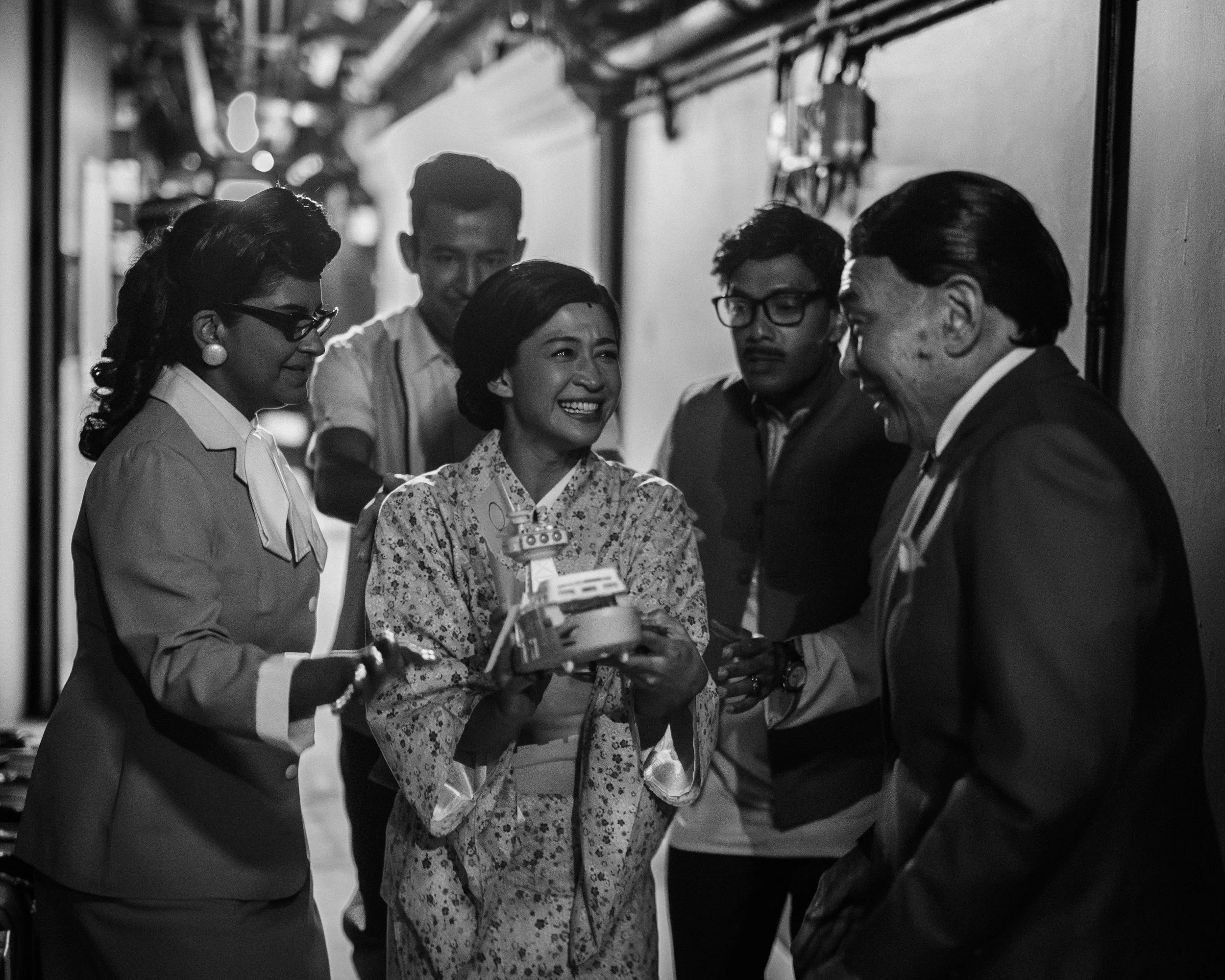 The cast of Scene 1955 give Munah a present as she exits from Scene 1945.