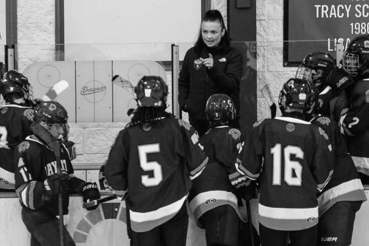 A female hockey coach giving instructions to young hockey players on the bench during a game or practice.