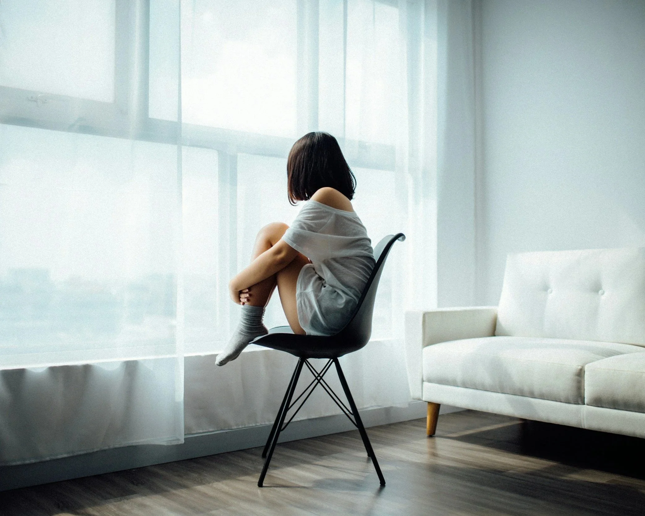 A woman sitting alone on a chair looking out a bright window, representing the search for clarity and healing from depression or difficult life transitions with a Nashville-area therapist.