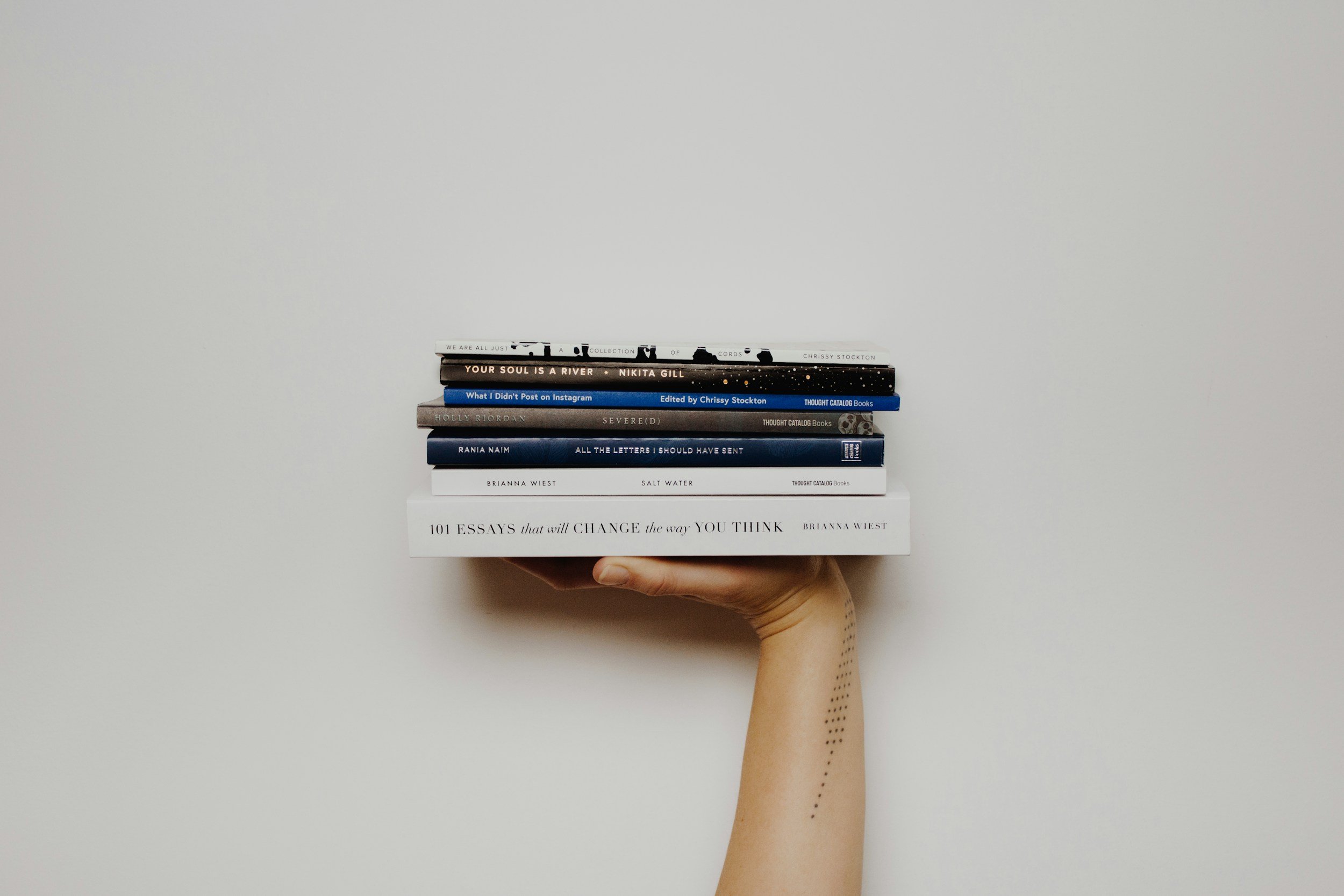 A hand holding a stack of ten books against a white background.