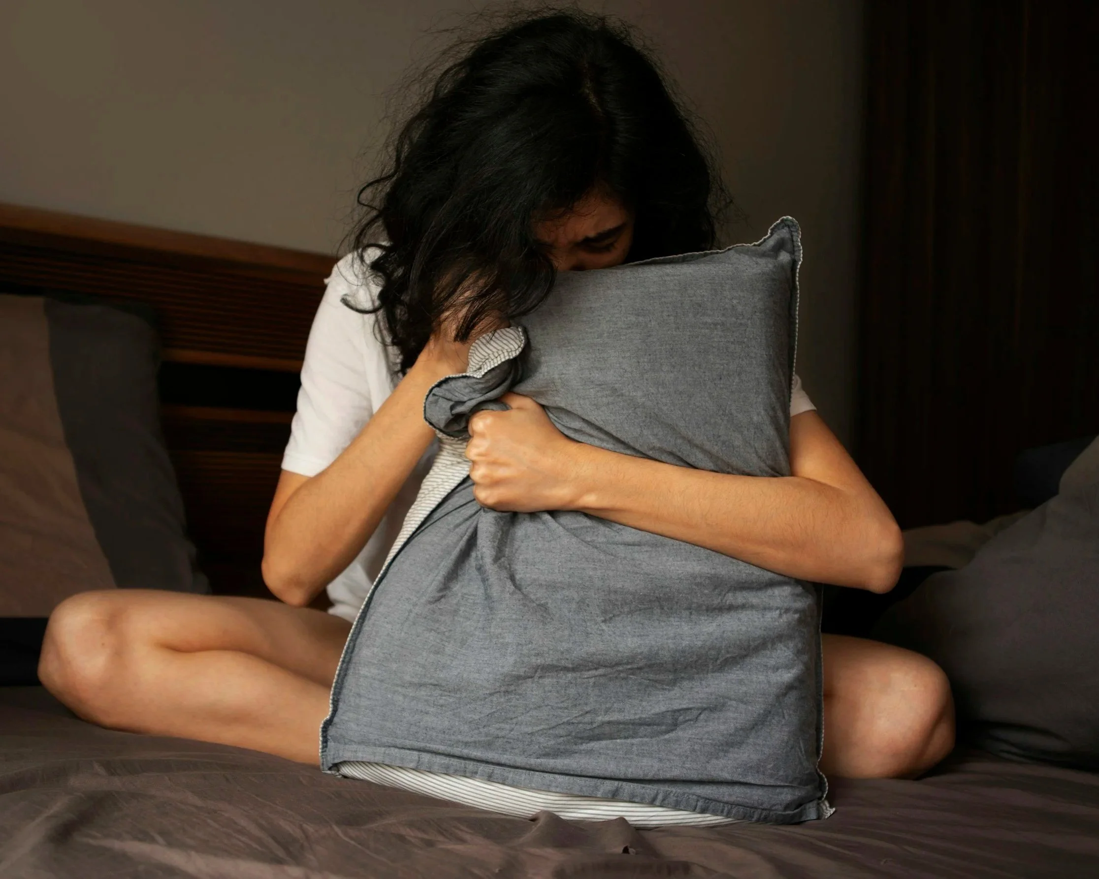 A distressed woman sitting on a bed hugging a pillow, illustrating the heavy emotional burden of anxiety and trauma that Daybreak Therapy helps clients overcome in Mt. Juliet, TN.