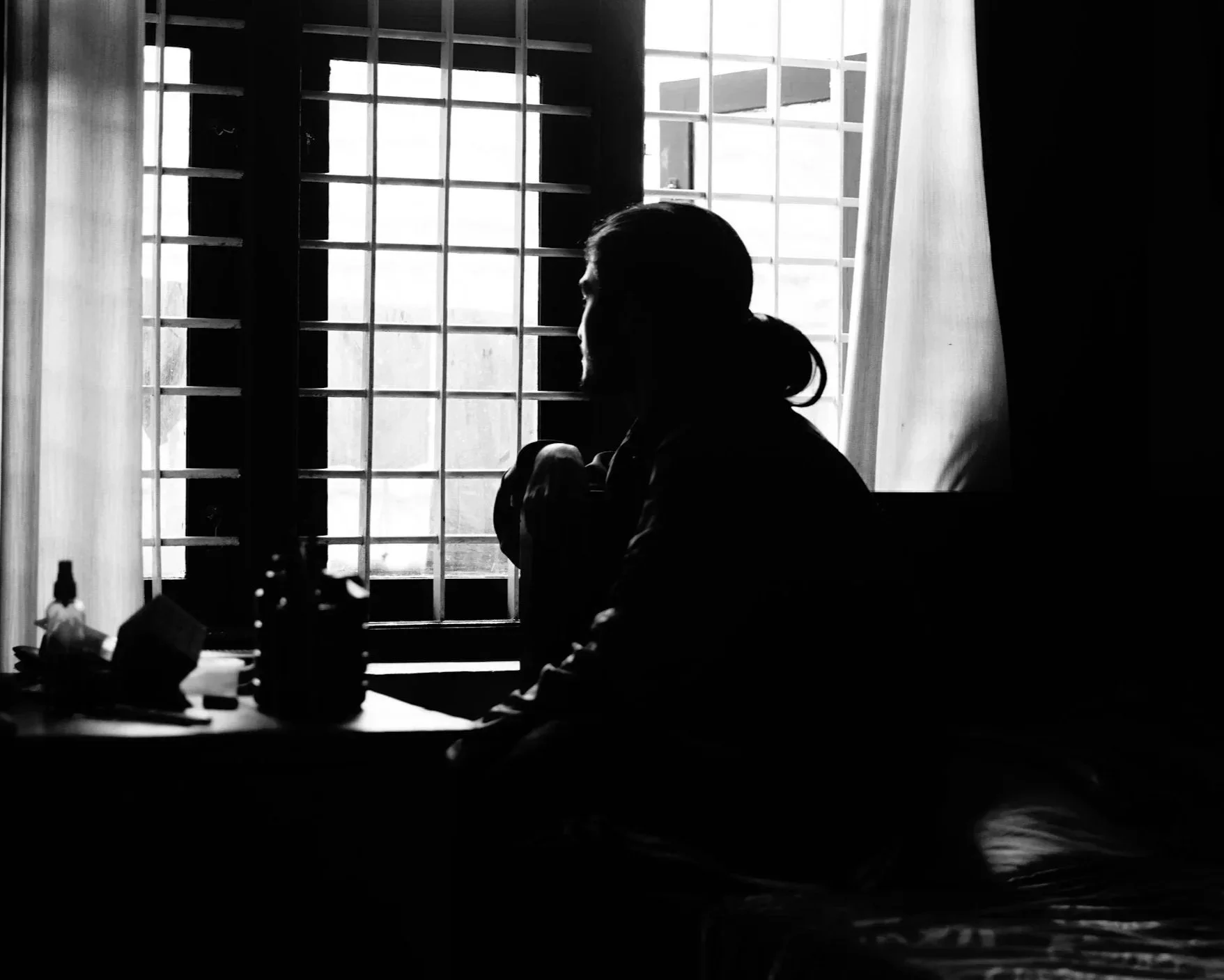 A dark silhouette of a person sitting alone by a window, representing feelings of isolation and the compassionate grief and depression counseling available at Daybreak Therapy.