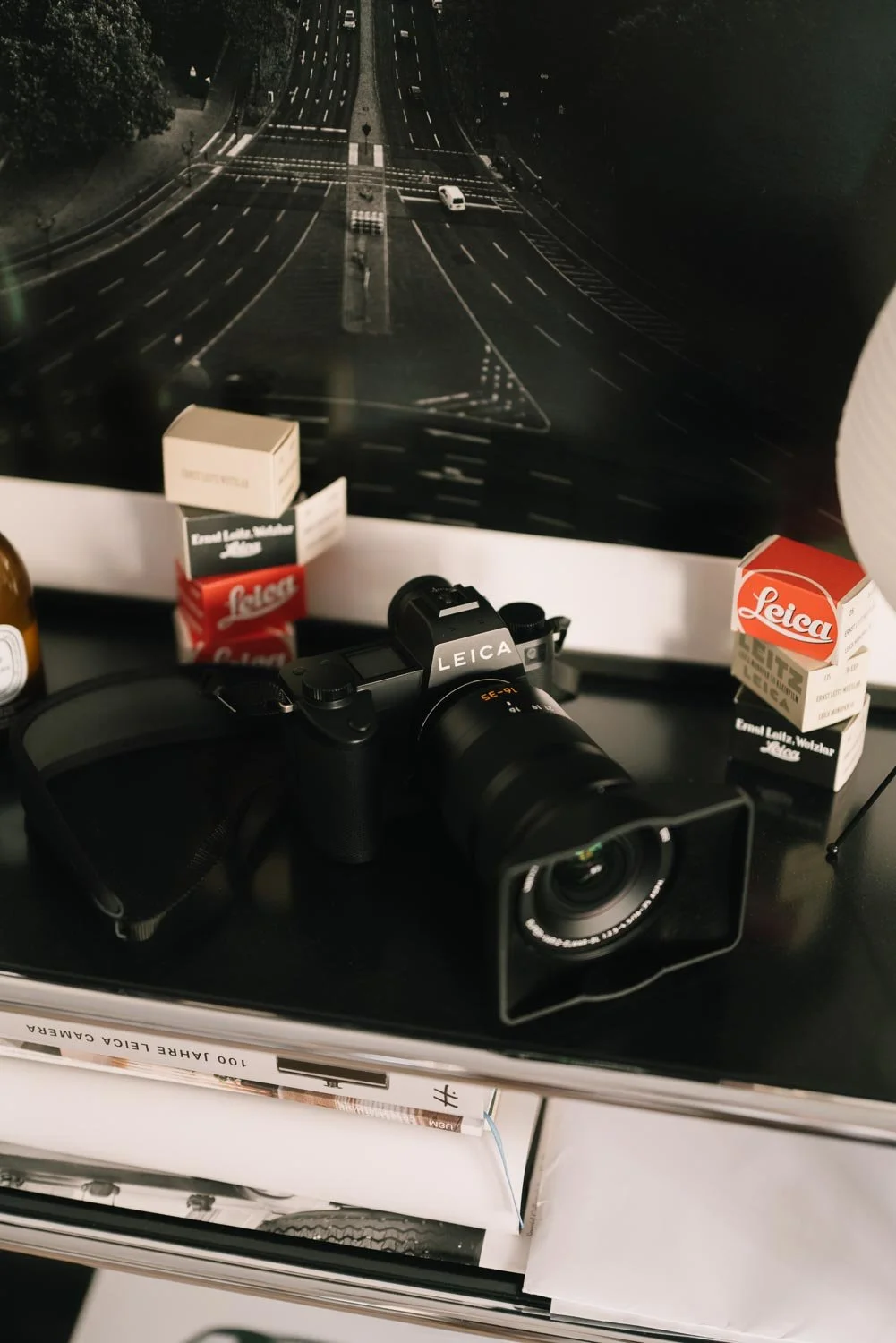 A Leica SL 3 P camera on a USM stall surrounded by leica film boxes with a printed photo in the background