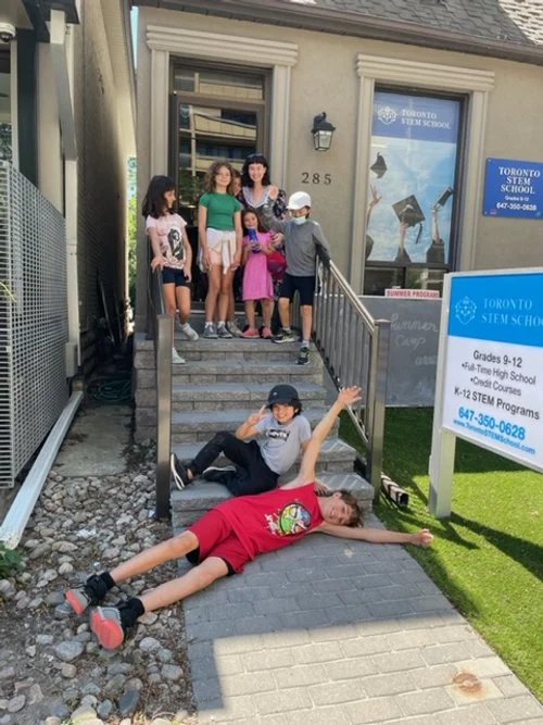 Young children sitting at desks in a classroom, working on laptops.