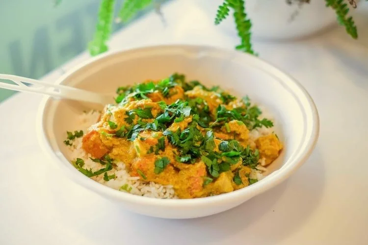 Bowl of white rice topped with yellow curry and chopped cilantro