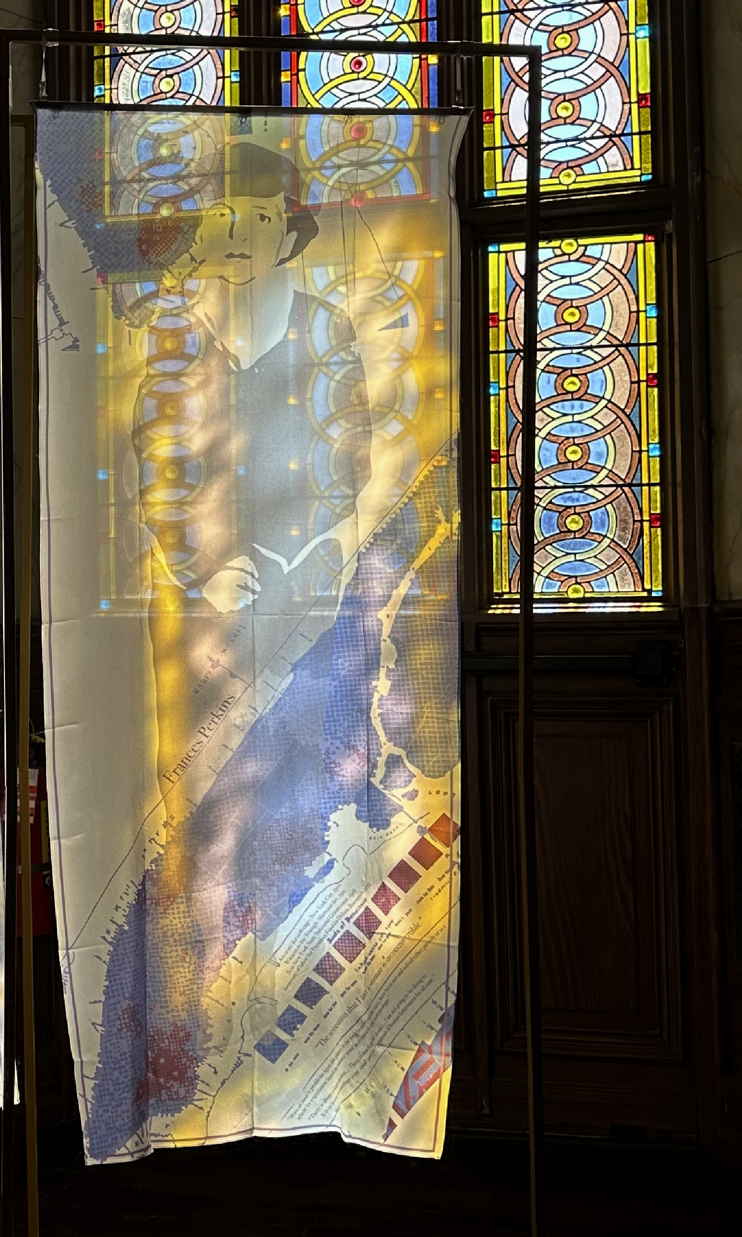 A fabric banner with a historic map and illustration of a woman, placed in front of stained glass windows with intricate circular patterns in various colors.