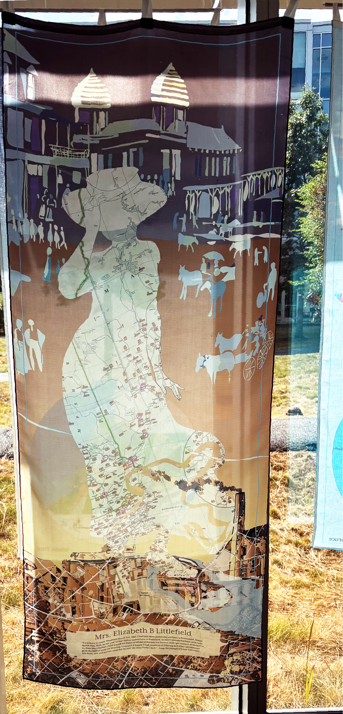 A decorative fabric banner with a map, couple of portraits, and illustrations of historical buildings, horses and carts, with a label at the bottom reading "Mrs. Elizabeth B Littlefield."