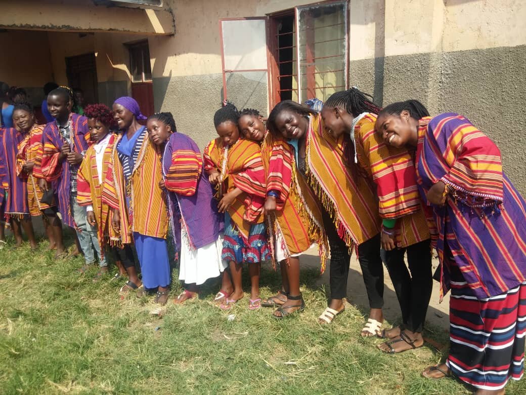 A group of people standing in a line, wearing colorful striped traditional garments, posing outside a building.