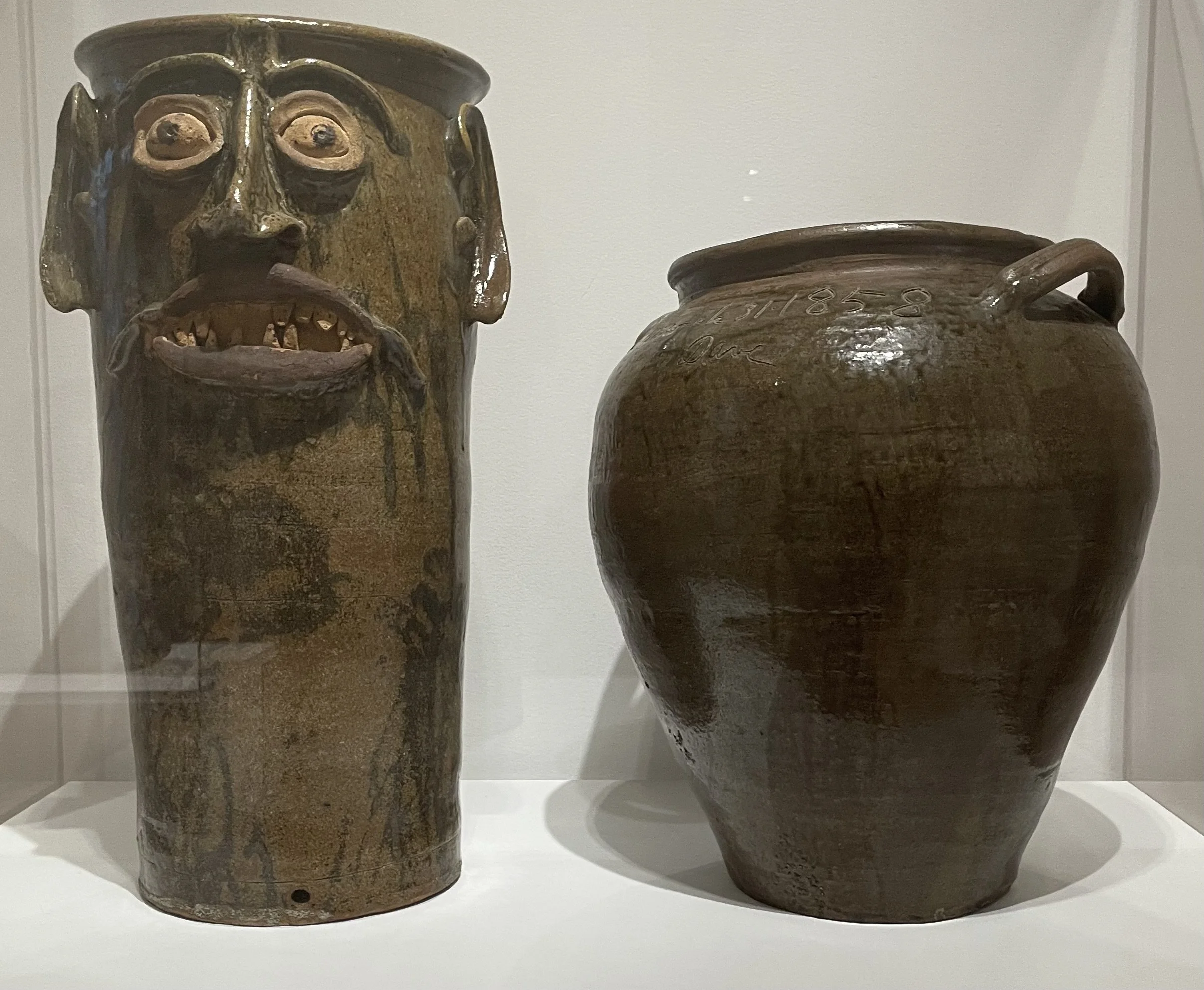 (Left) Face Jar, ca. 1870. Alkaline-glazed stoneware and unglazed porcelain. (Right) David Drake, Jar. 1858. Alkaline-glazed stoneware.