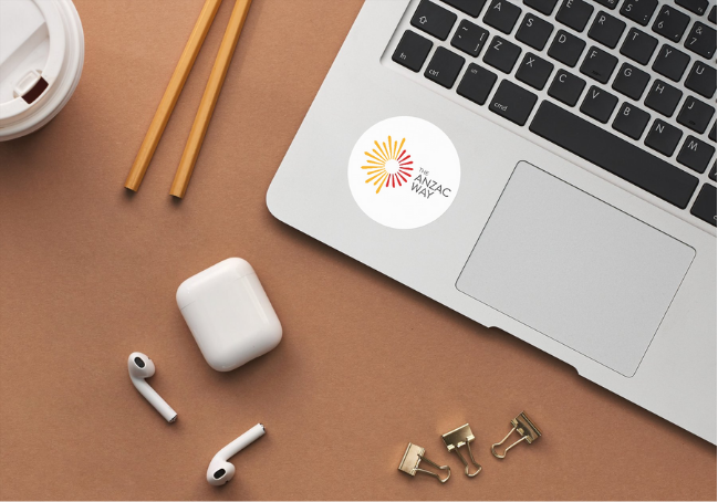 Laptop with ANZAC Day sticker, wireless earbuds, paper clips, a cup, and wooden chopsticks on a brown surface.