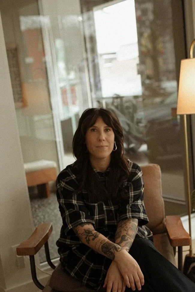 Woodside Holistic founder Kristen Blow sitting on a chair by a window in a cozy cafe.