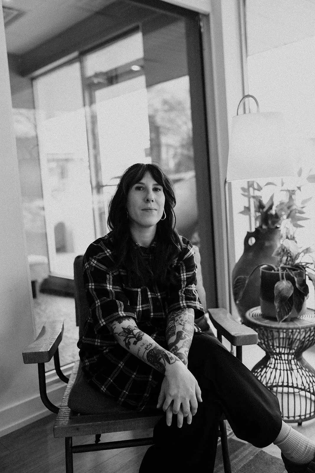 Woodside Holistic founder Kristen Blow sitting on a chair by a window in a cozy cafe.