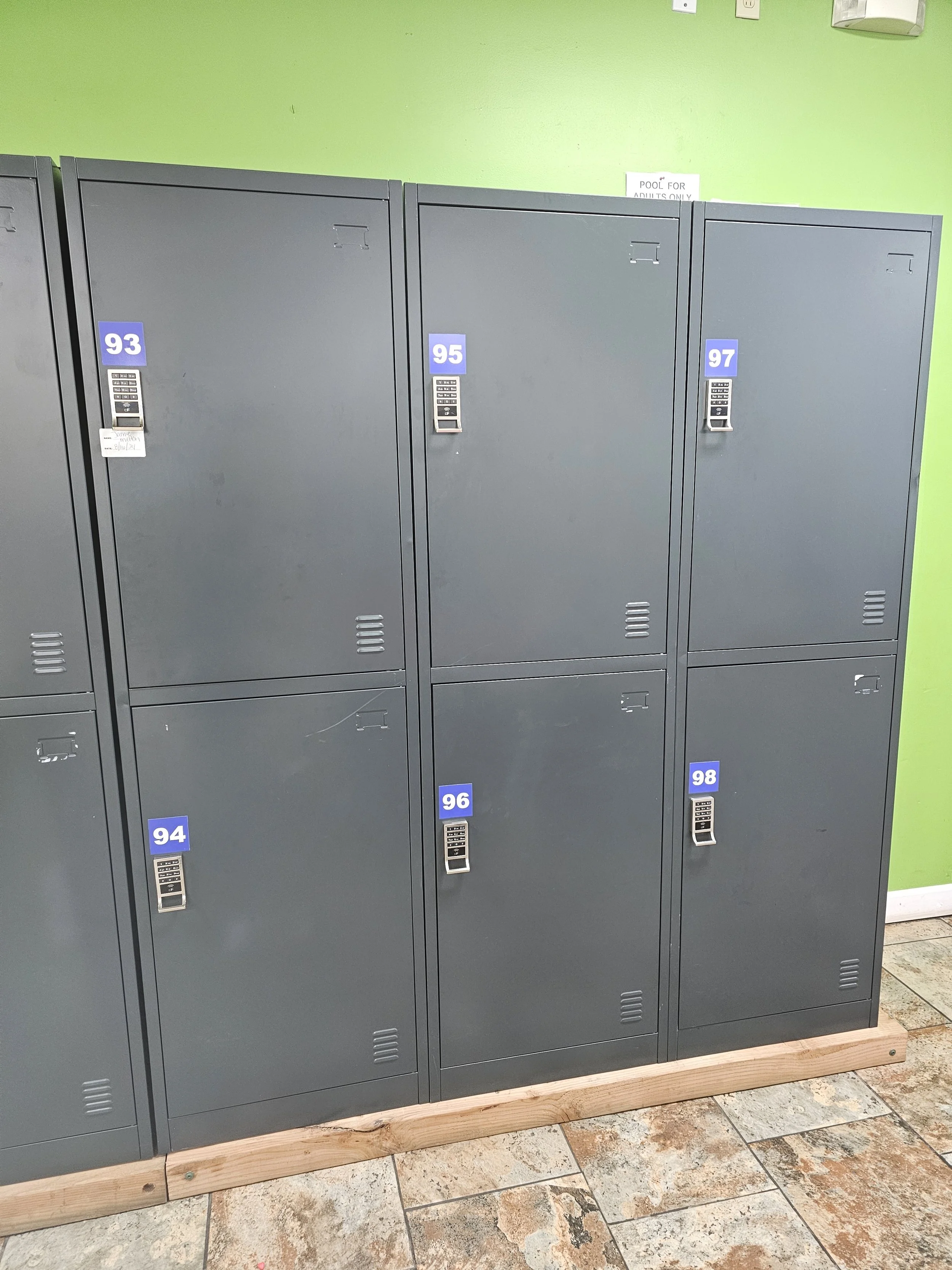 Row of gray lockers with digital locks against a green wall.