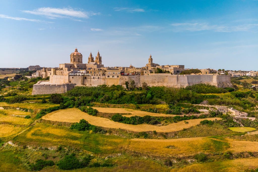 A historic fortress and cathedral on a hilltop with surrounding green fields and clear blue sky.