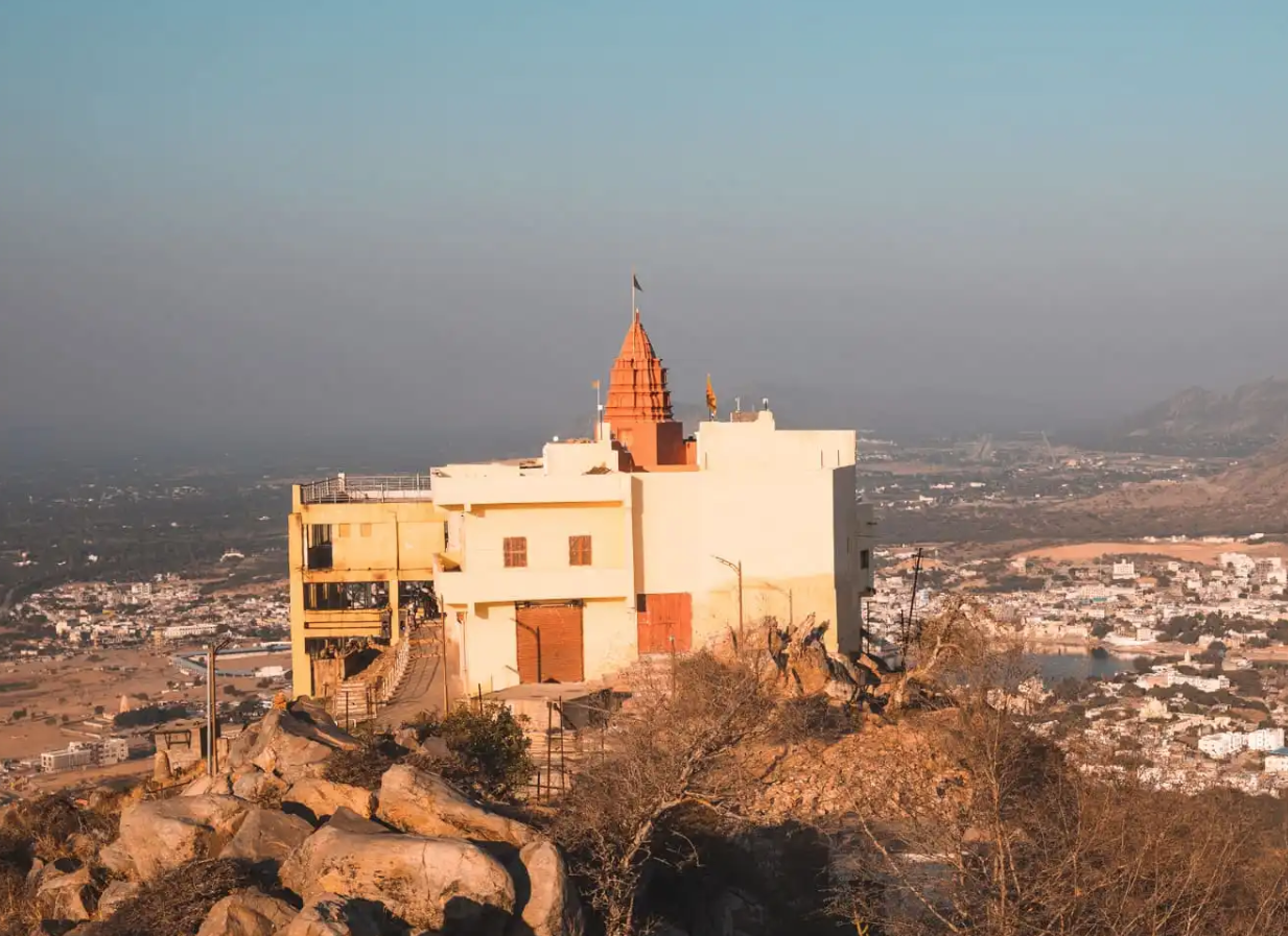 Temple structure atop a hill in India overlooking a cityscape with mountains in the background.