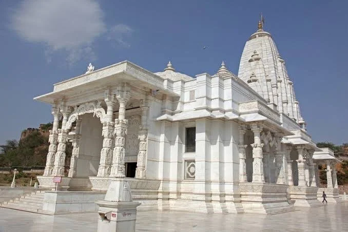 A white Hindu temple with intricate carvings and a tall shikhara (temple tower) against a blue sky.