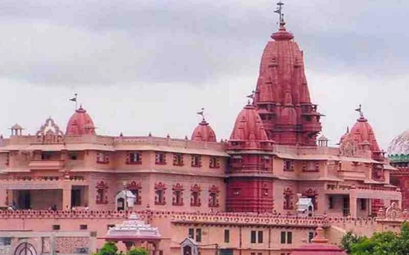 A large pink sandstone Hindu temple with multiple spires and intricate carvings, against a cloudy sky.