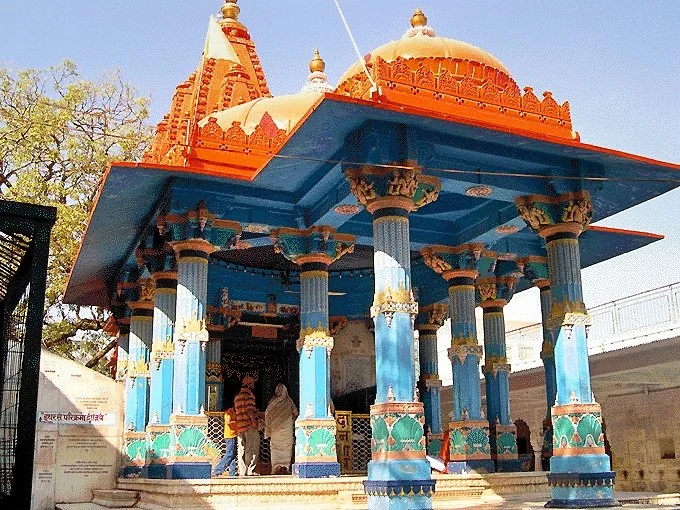 Colorful Hindu temple with blue pillars and orange domed roof, visitors entering the temple.