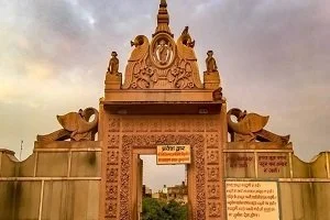 Ornate temple entrance with detailed carvings and sculptures, flanked by decorative walls and a cloudy sky in the background.