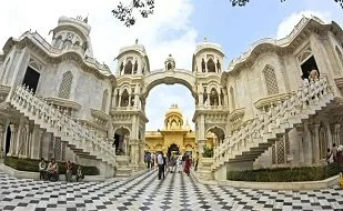 View of a grand, ornate historical palace with white and gold domes, staircases on both sides, and visitors walking in the courtyard.