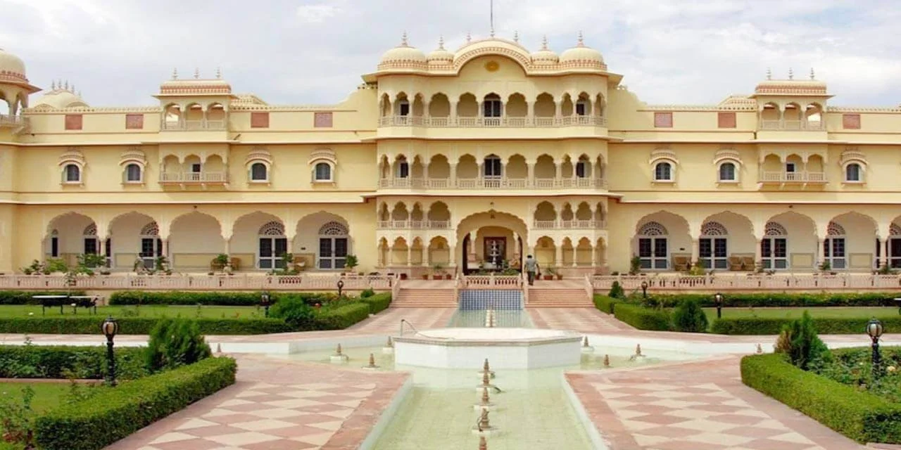 Large, ornate cream-colored palace with multiple balconies and domes, surrounded by well-maintained gardens and a fountain in the front.