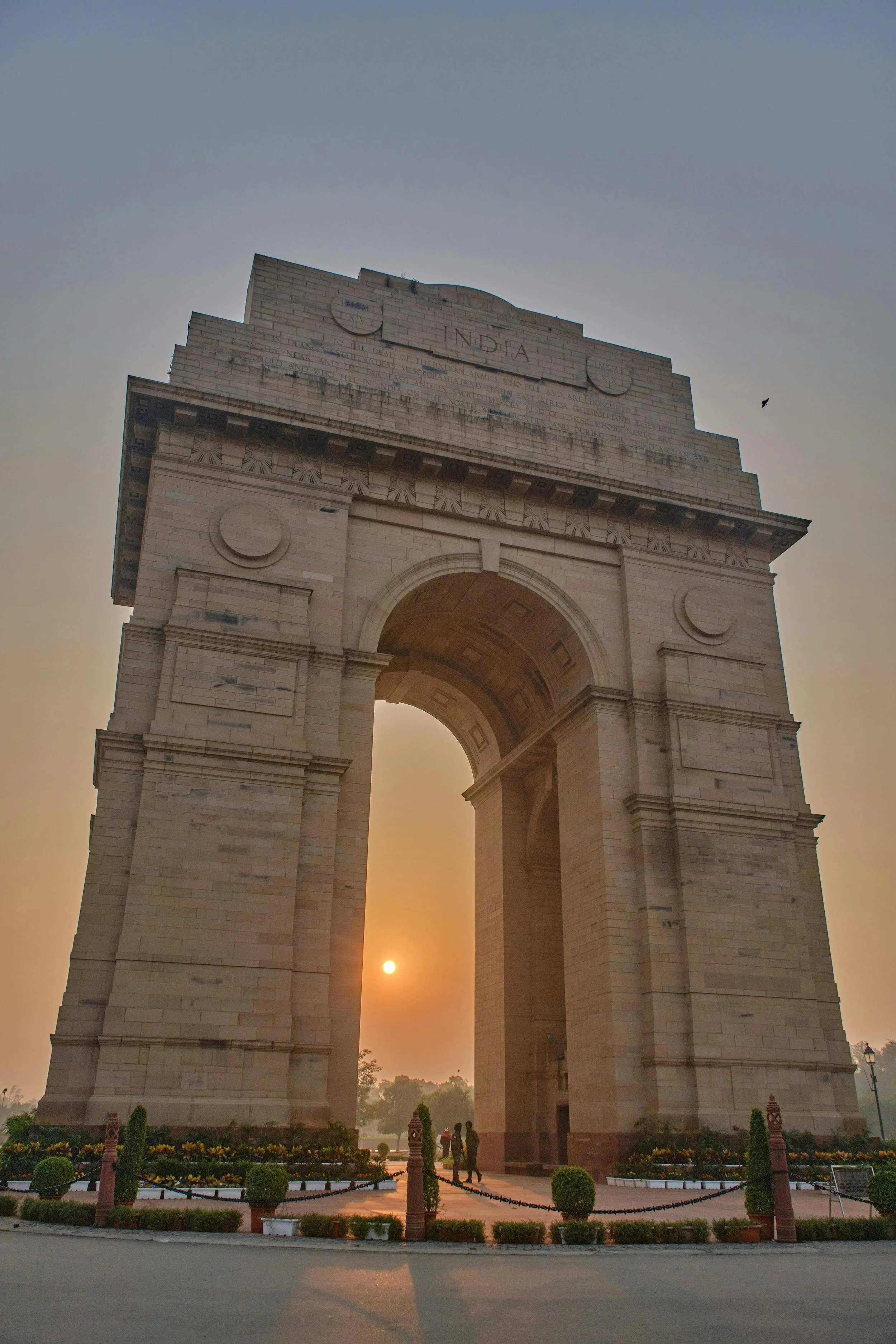India Gate monument during sunrise with two people walking nearby.