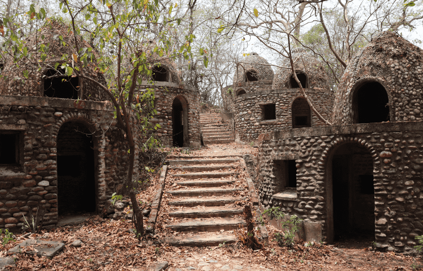 A set of stone stairs leading to multiple cobblestone structures with arched doorways and windows, surrounded by leafless trees and fallen leaves.