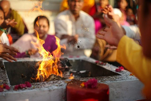 People gathered around a sacred fire during a religious ceremony, with some hands reaching towards the fire and others observing.