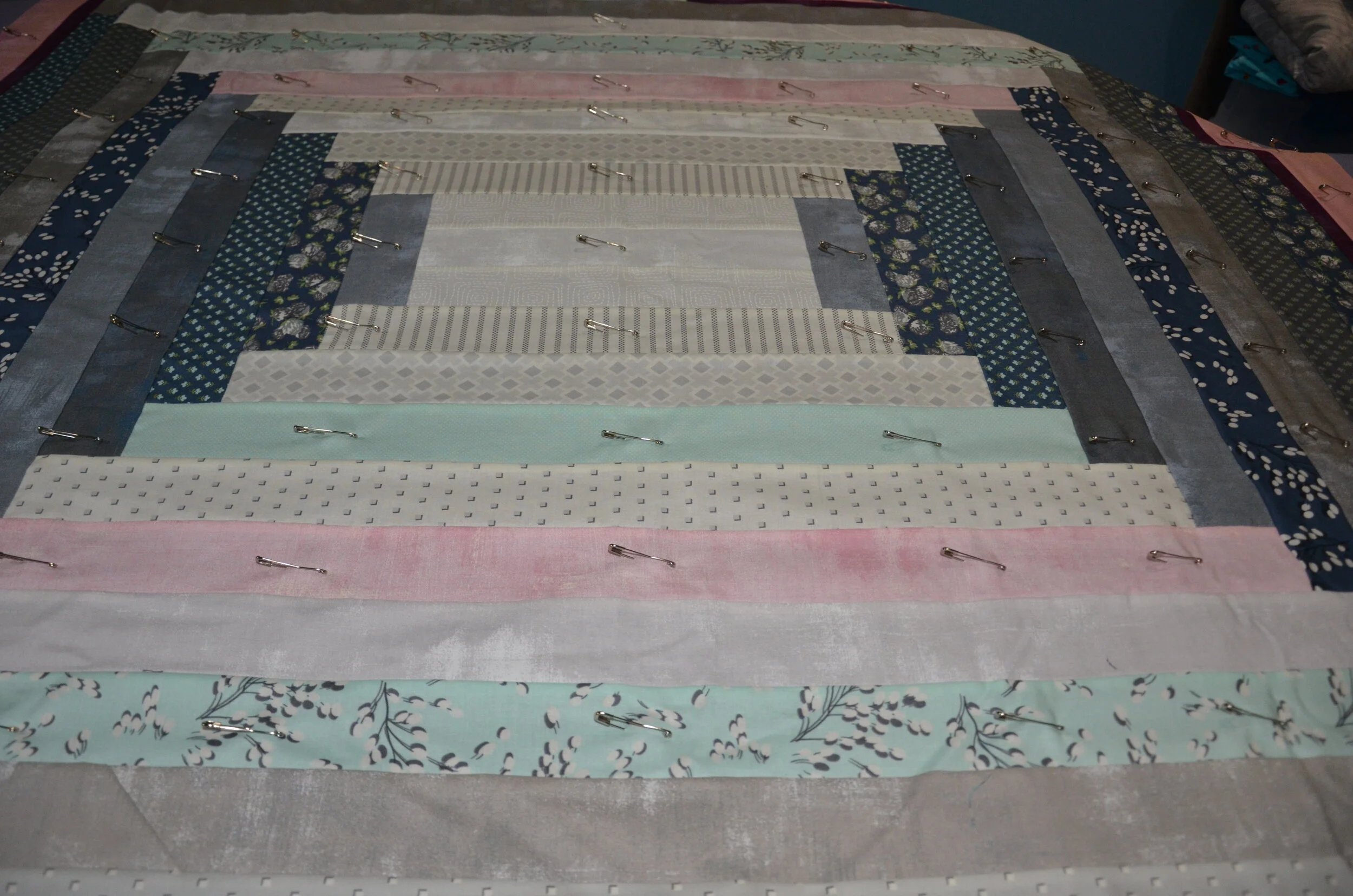 A quilt with a pinned surface. The fabric features floral, polka dots, stripes, and solids.