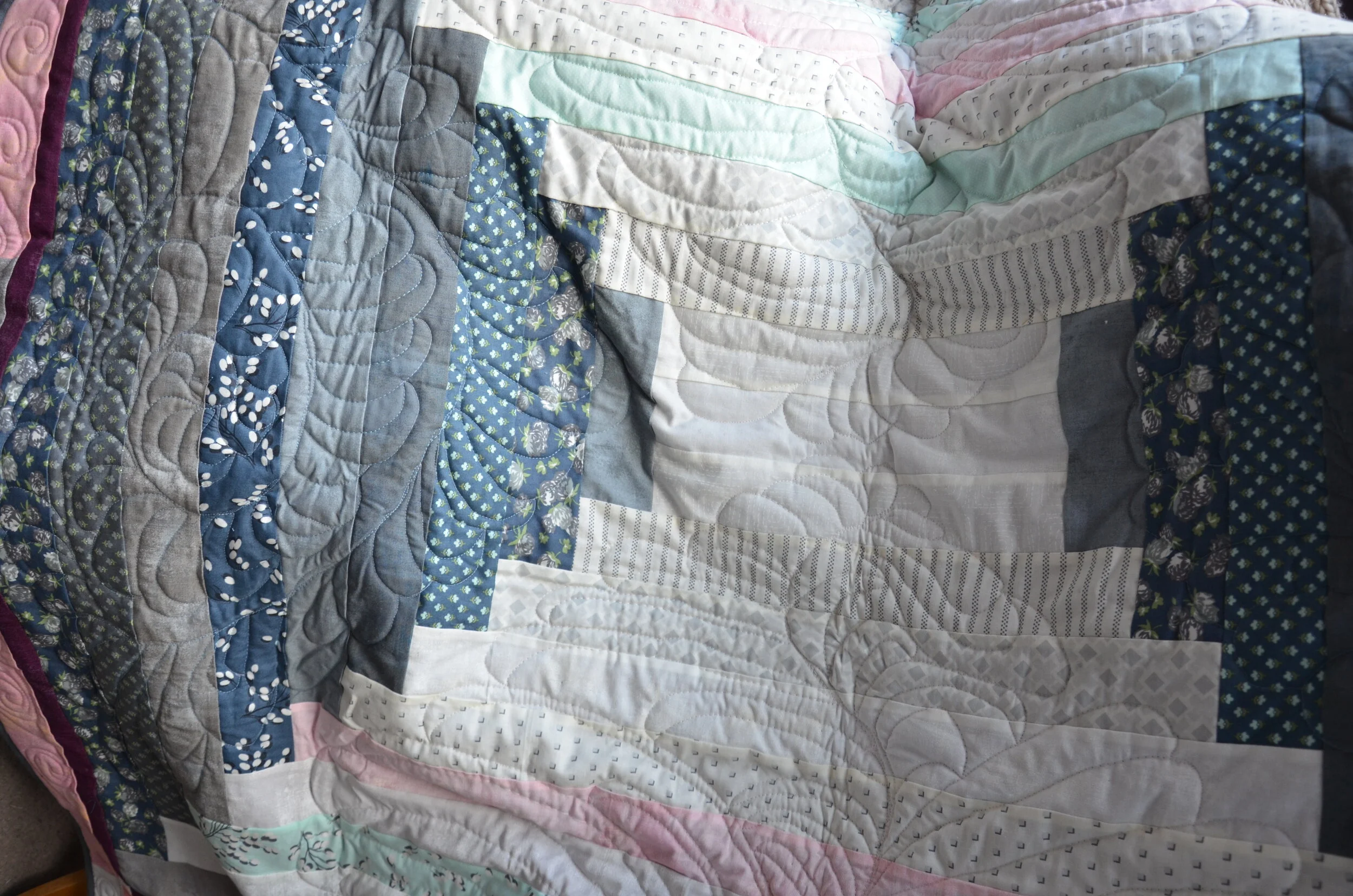 a finished quilt with pastel fabric pieces, featuring quilting stitches.