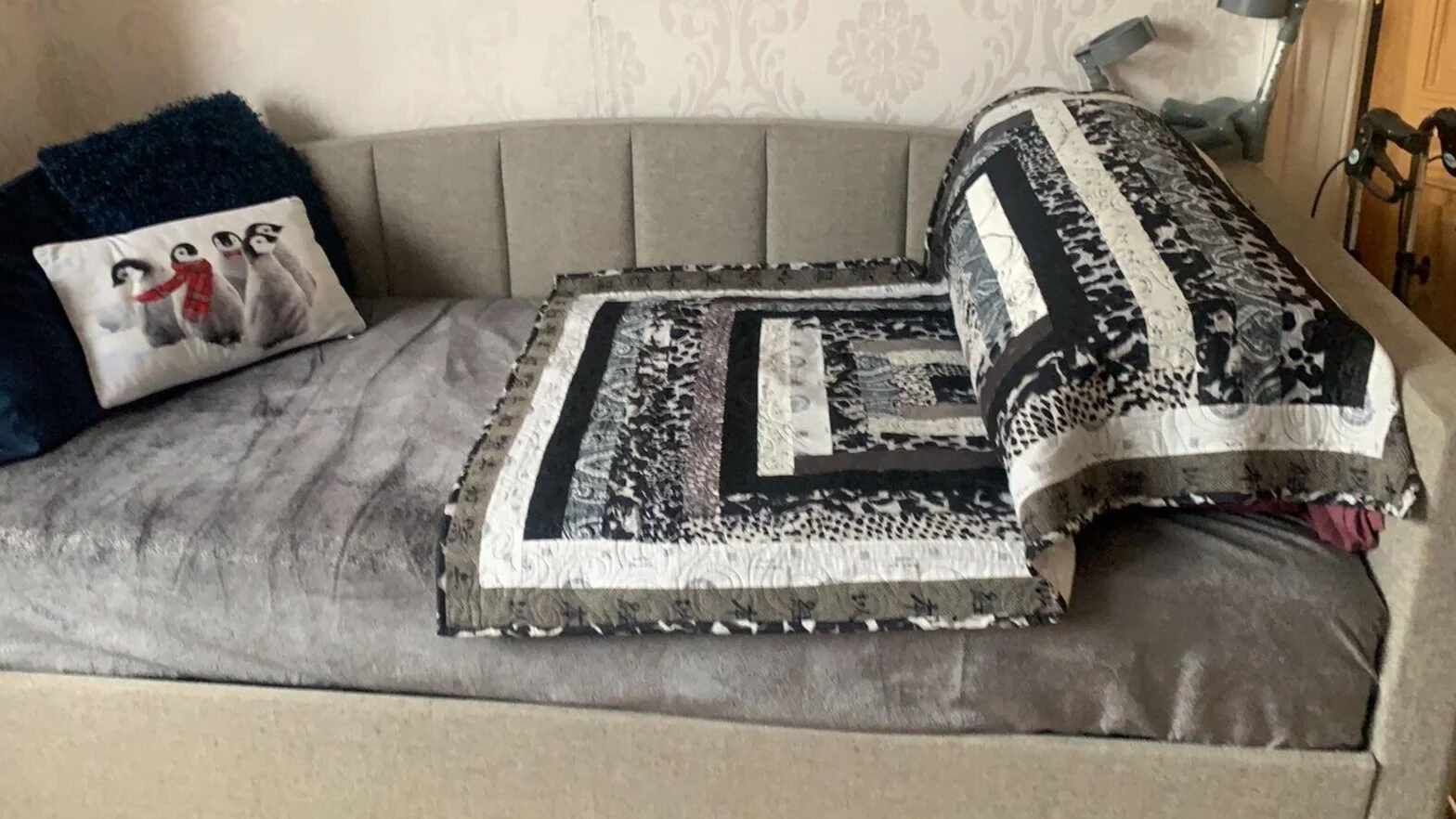 A sofa with a black, white, and grey quilt draped over the arm.