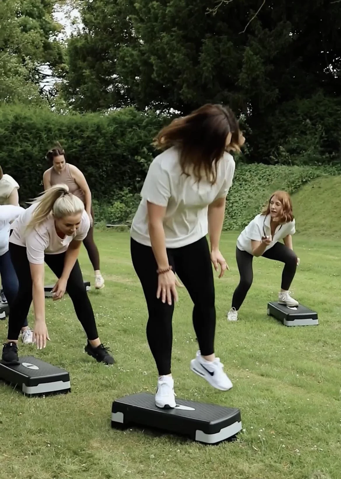 Group of women exercising outdoors on a grassy field, using step platforms for a workout.