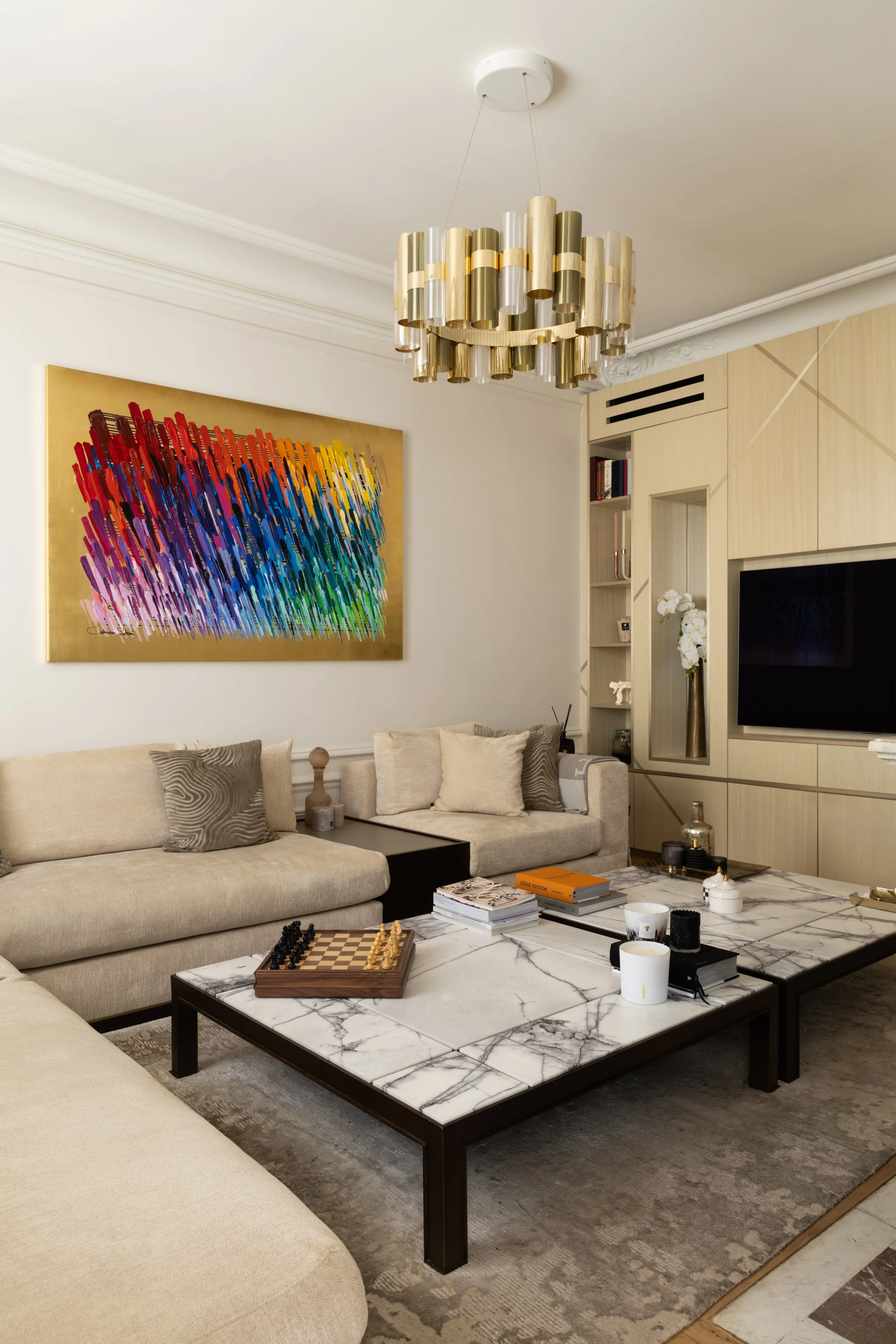 Salon TV du projet Malesherbes à Paris, avec canapé beige, tables basses en marbre veiné, tableau coloré et suspension dorée — Intérieurs Chomet.