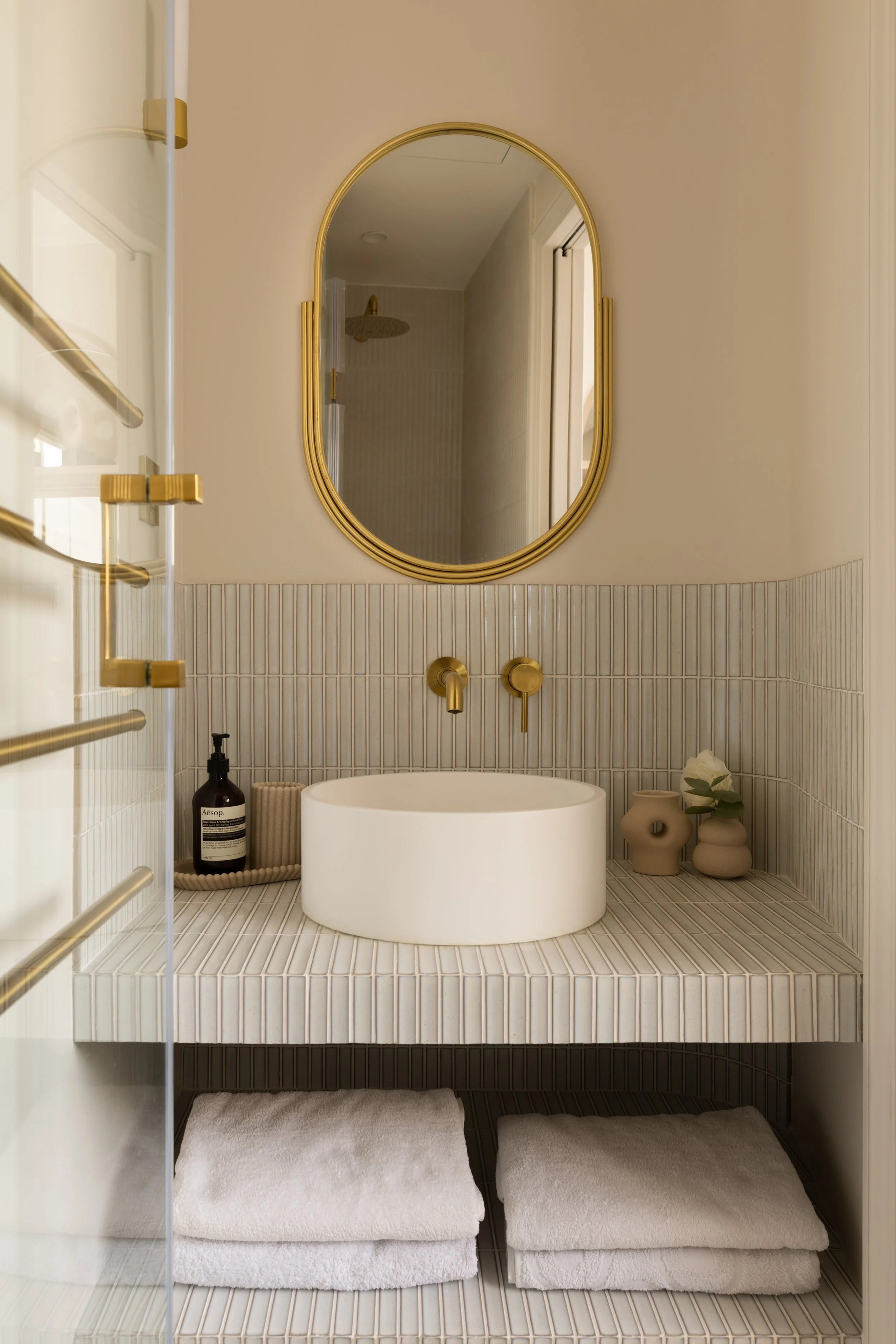 Salle d’eau contemporaine avec vasque ronde, miroir doré et carrelage texturé.