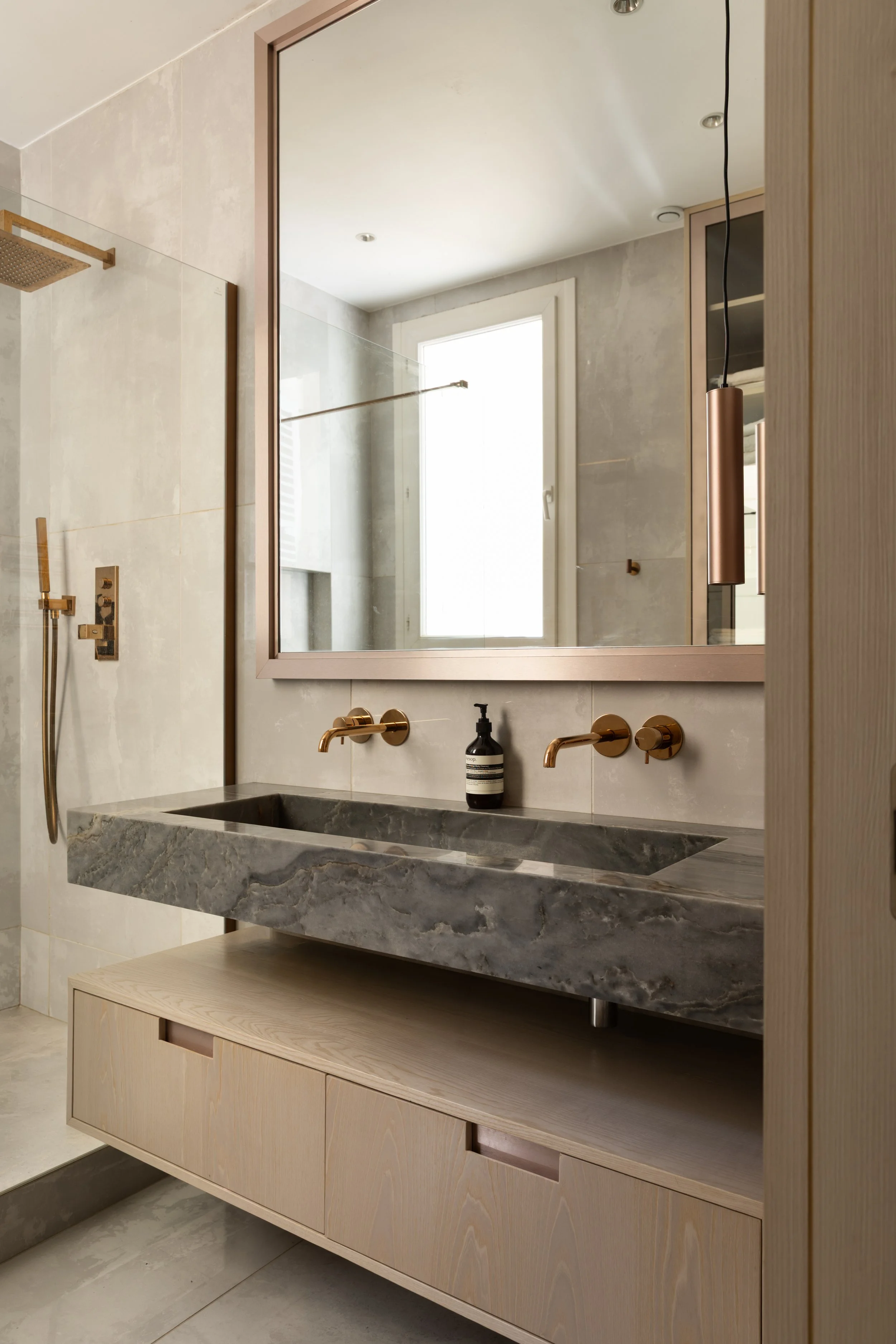 Salle de bain du projet Malesherbes à Paris, avec double vasque en pierre grise veinée, meuble suspendu en bois clair, grand miroir et robinetterie dorée — Intérieurs Chomet.