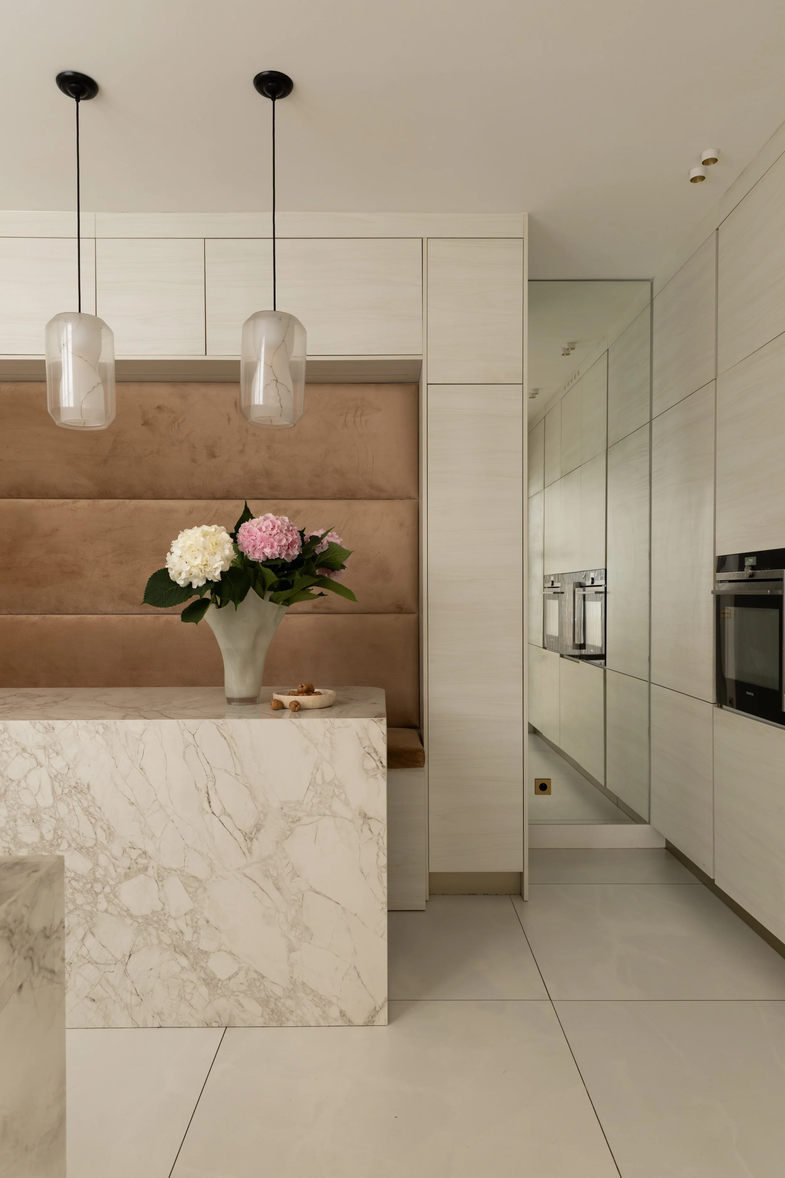 Espace repas de la cuisine du projet Malesherbes à Paris, avec banquette capitonnée camel, table en pierre veinée, suspensions et rangements en bois clair — Intérieurs Chomet.